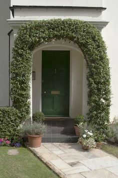 a green door in front of a white house with potted plants on the side