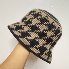 a hand is holding a knitted hat with black and tan designs on it,