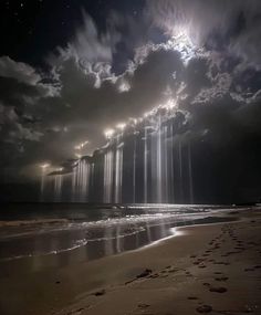 the sun is shining through clouds over the water at night on an empty beach with footprints in the sand