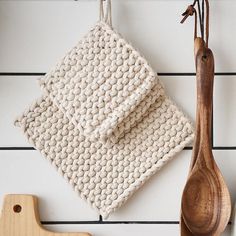 two wooden spoons and a white knitted dishcloth hanging on a wall next to a cutting board