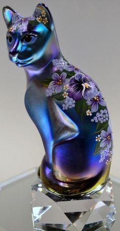 a cat figurine sitting on top of a crystal base with flowers painted on it