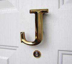 the letter j is attached to a door handle on a white door with gold trim