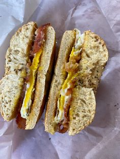 two halves of a sandwich with bacon and egg on it, sitting on wax paper