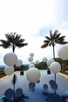 an outdoor swimming pool with white balloons floating in the air and palm trees behind it