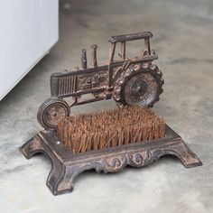 a metal sculpture of a tractor with a brush in it's holder on the floor