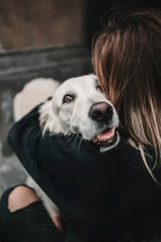 a woman is hugging her dog outside on the street with it's face close to her chest