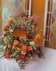 an arrangement of flowers on a table in front of a stained glass window at a wedding