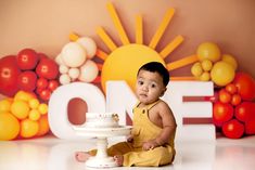 a baby sitting on the floor with a cake in front of him and an orange background