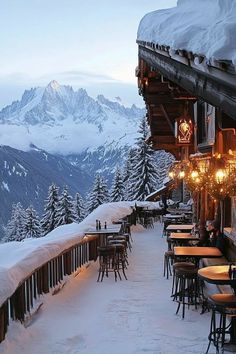 an outdoor restaurant with tables and chairs covered in snow, overlooking the mountains at dusk