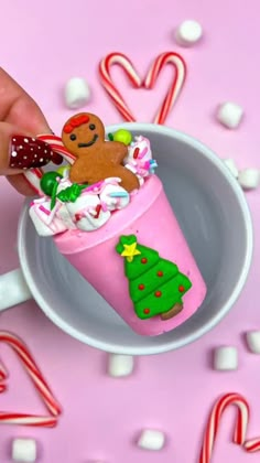 a hand is holding a cup filled with candy canes and marshmallows