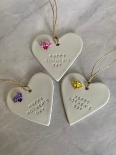 three heart shaped ceramic ornaments with happy mothers day written on the front and two small flowers at the bottom