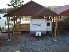 an rv parked under a wooden structure next to a body of water with trees in the background