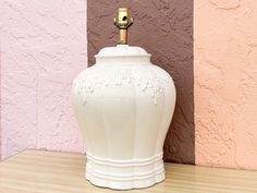 a white vase sitting on top of a wooden table next to a pink and purple wall