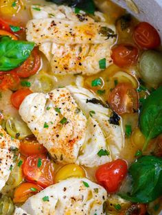 some fish and vegetables are in a white bowl on the table with tomatoes, basil