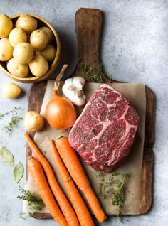 raw meat, carrots and potatoes are on a cutting board next to a wooden spoon