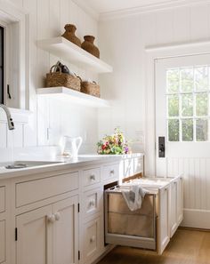 a kitchen with white cabinets and open shelving on the wall above the sink is filled with flowers