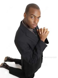 a man in a suit sitting on the ground with his hands clasped to his chest