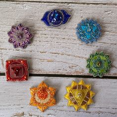 six different colored brooches sitting on top of a white wooden table next to each other