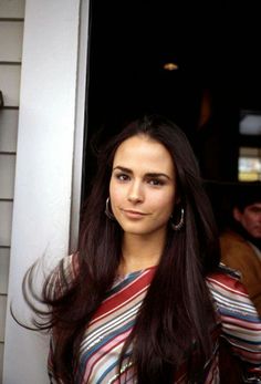 a woman standing in front of a door with long dark hair and wearing a striped shirt