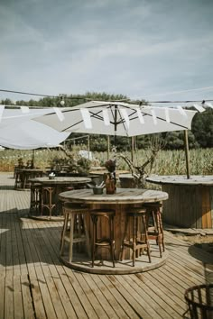 an outdoor patio with tables and umbrellas on the wooden flooring, surrounded by tall grass