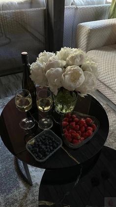 a table topped with two wine glasses filled with fruit and flowers next to a bottle of wine