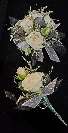 two bouquets of white roses and greenery on a black tablecloth with ribbons