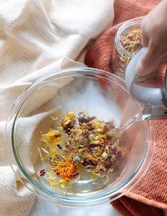 someone is pouring tea into a glass bowl with dried flowers in it and on top of a towel