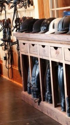 several pairs of riding boots are lined up on a bench in a shop with many different types of helmets