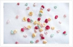 small crocheted flowers are scattered on a white surface, including red, yellow and green