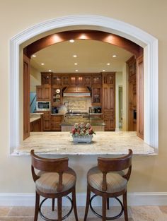 two stools sit at the center of a kitchen island with an arched doorway leading into it