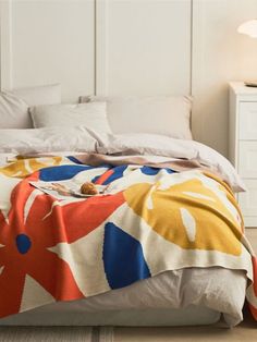 a bed with a colorful blanket on top of it next to a night stand and lamp