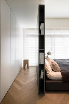 a bed sitting next to a book shelf on top of a hard wood floor in a bedroom