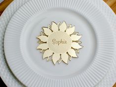 a white plate topped with a gold sunflower on top of a wooden table next to a knife and fork