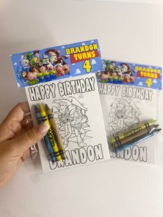 a hand holding two coloring books with cartoon characters on them