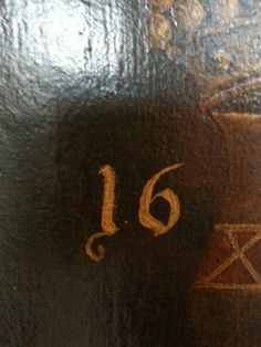 the number sixteen is written in gold on a black leather surface with red and yellow designs