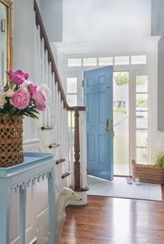 a blue front door with pink and white flowers in a basket on the floor next to it