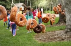 several donuts are hanging from strings in the grass, with people standing around them