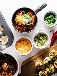 an overhead view of food in bowls on a cutting board with utensils next to it