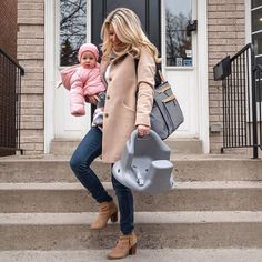 a woman holding a baby in her arms while standing on the steps outside of a house