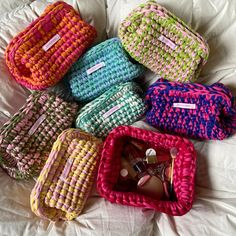 six woven bags sitting on top of a white bed next to each other, all in different colors