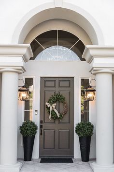 a front door with two large planters and a wreath on the side of it