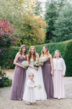 a group of women standing next to each other in front of some bushes and trees