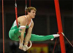 a man in green pants and white shirt doing aerial tricks on a pole with red bars