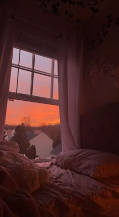 the sun is setting in front of a window that has curtains on it and there is a bed with an unmade comforter