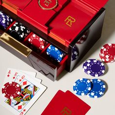 a red box filled with playing cards next to poker chips and dices on top of a table