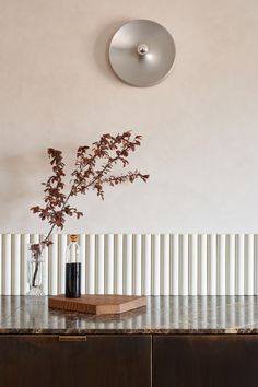 a vase with some flowers on top of a wooden table next to a wall mounted light