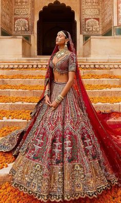 a woman in a red and gold bridal gown standing on steps with flowers all around her