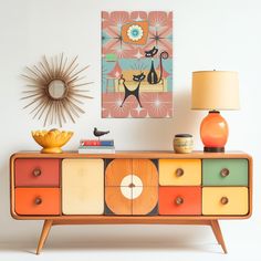 an orange and yellow dresser with two lamps on it next to a wall mounted painting