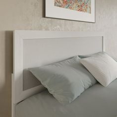 a bed with two pillows on top of it and a painting above the headboard