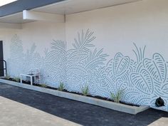 a white building with a planter in front of it and a wall that has plants painted on it